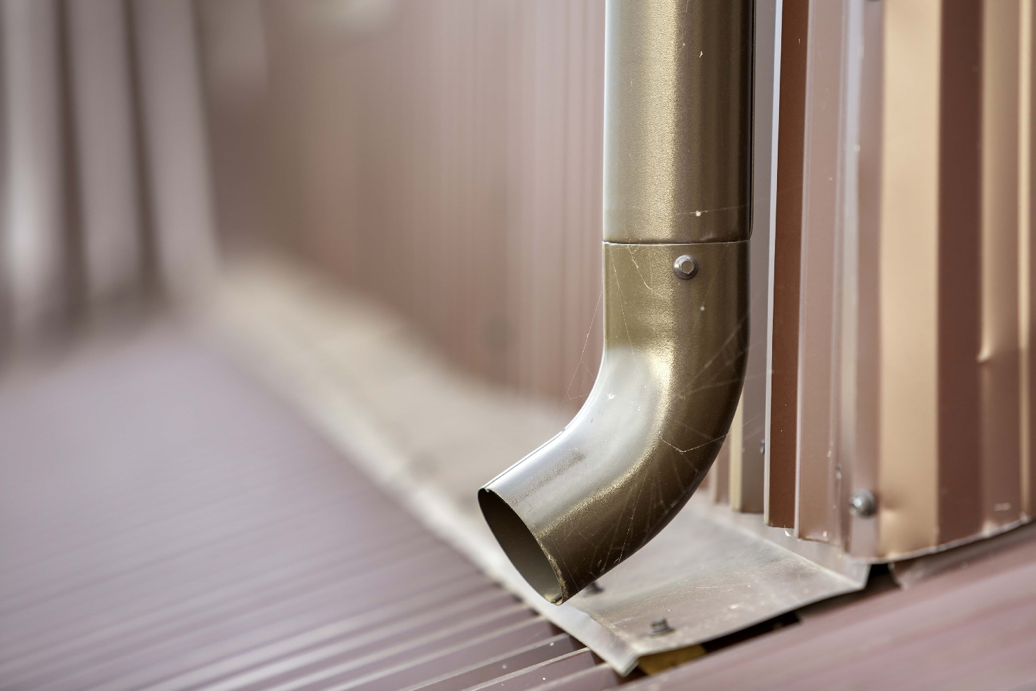 Close-up of brown new gutter metal system pipe on blurred copy space background. Vertical construction for draining rain water from building roof on the wall. Drain protection, professional work.
